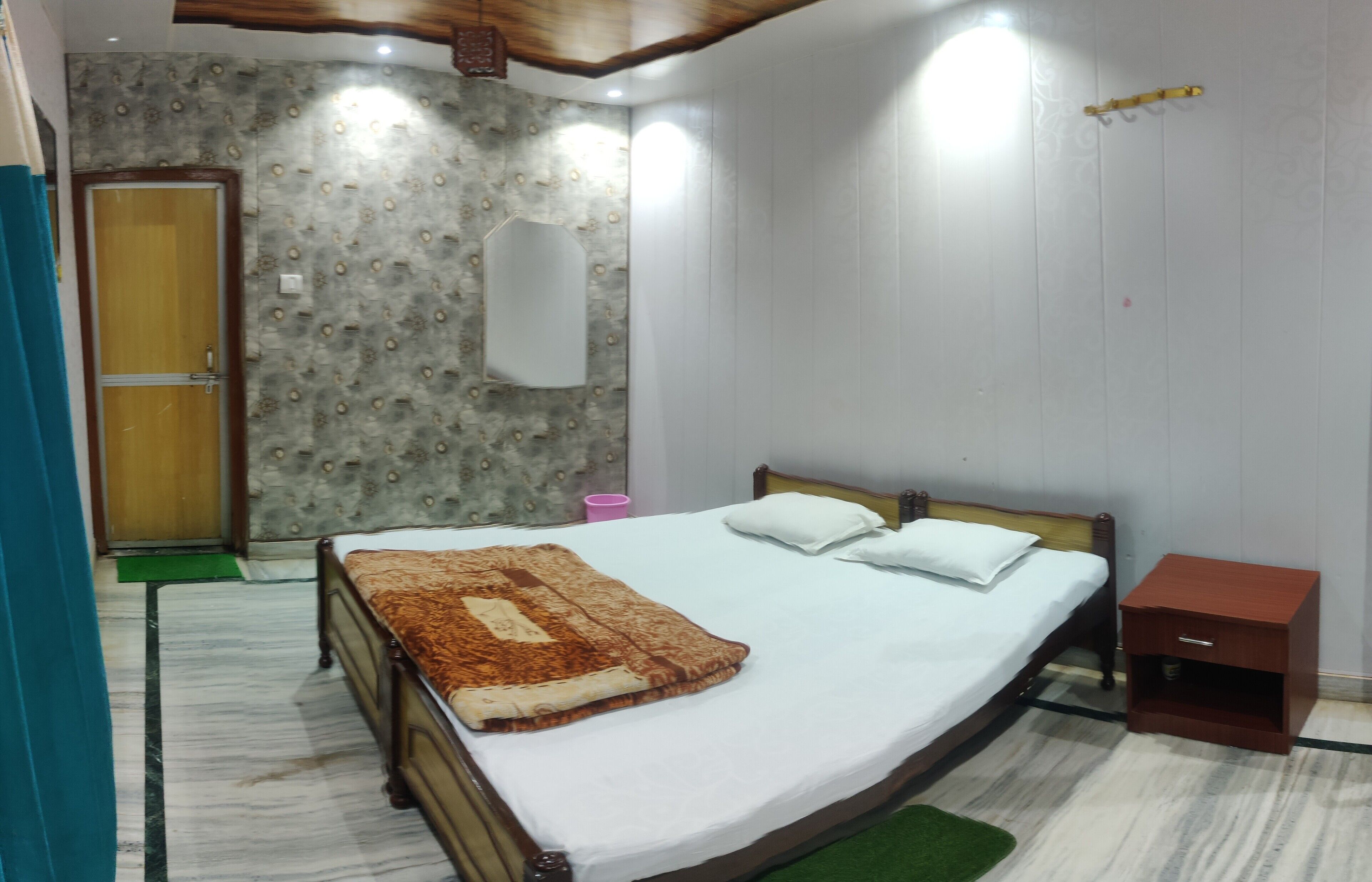 Quarto com cama, mesa de cabeceira de madeira, espelho e porta.