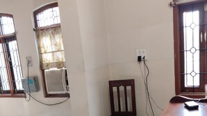 Una habitación con una mesa de vidrio, una silla de madera, un escritorio de madera y una ventana con reja de metal.