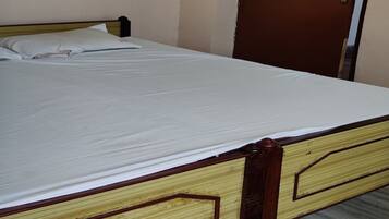 Una cama individual con estructura y cabecera de madera, una puerta marrón con placa de número y una pequeña estantería sobre la cama.