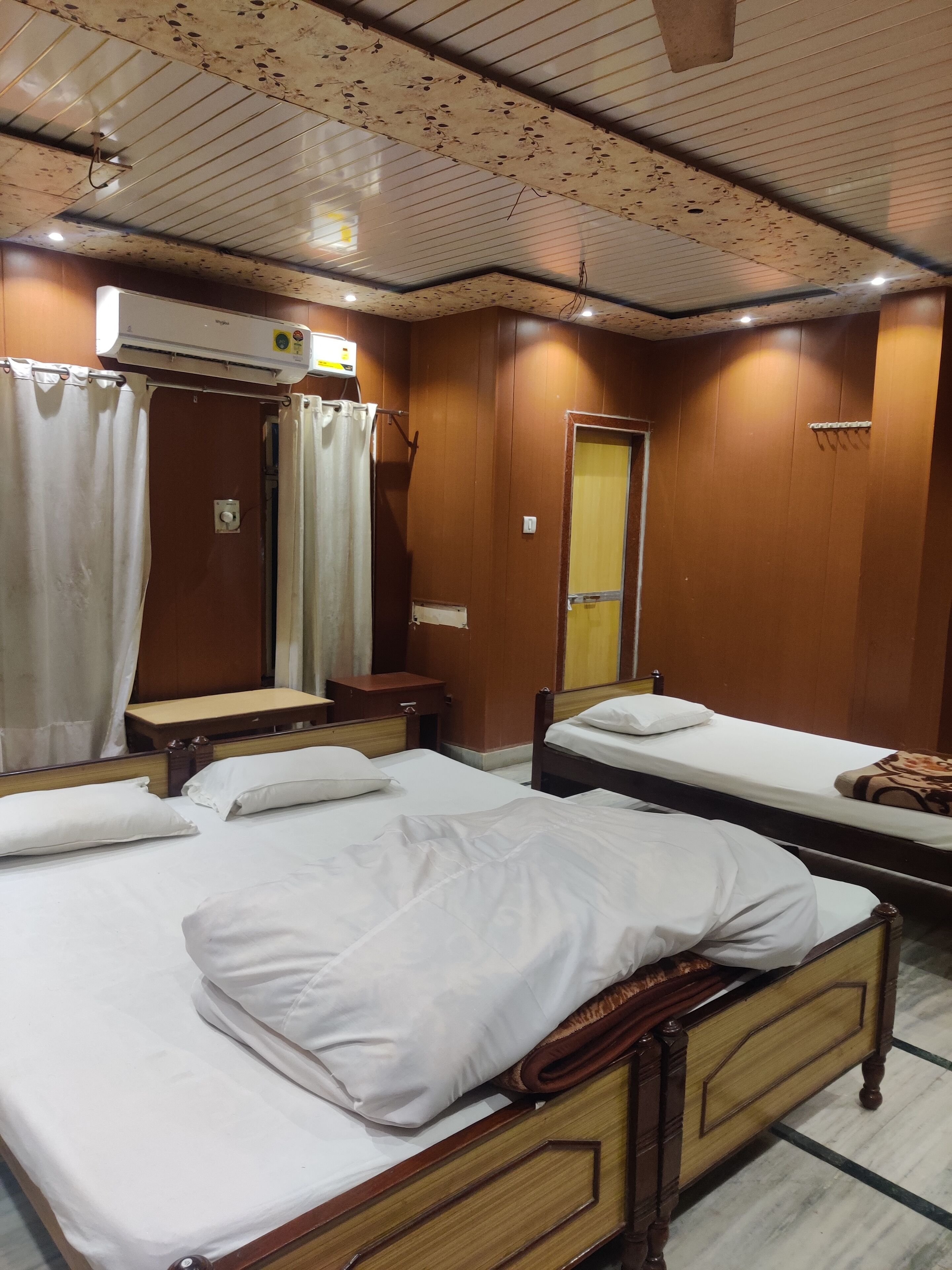 A hotel room with two single beds, a wooden headboard, a bedside table, a mirror, and a wardrobe.