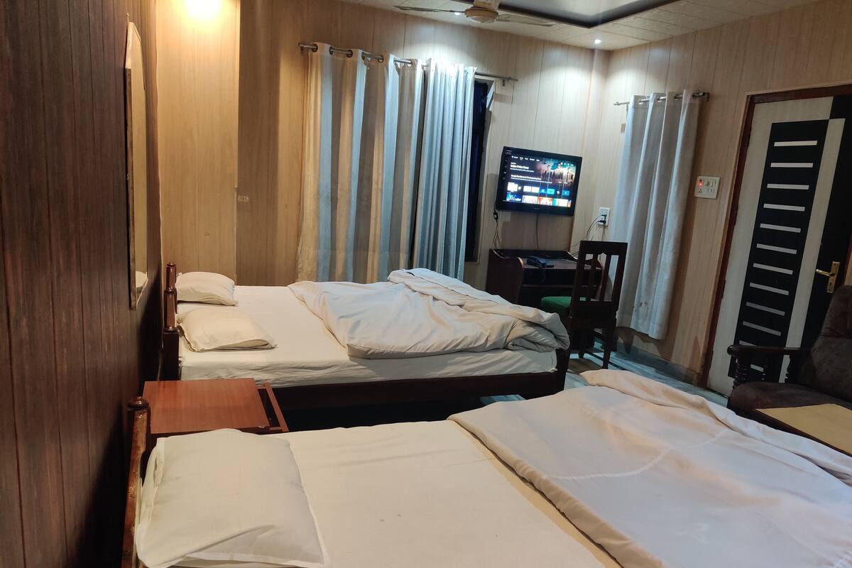 Hotellihuone, jossa on kaksi sänkyä, työpöytä, televisio ja tuoli.