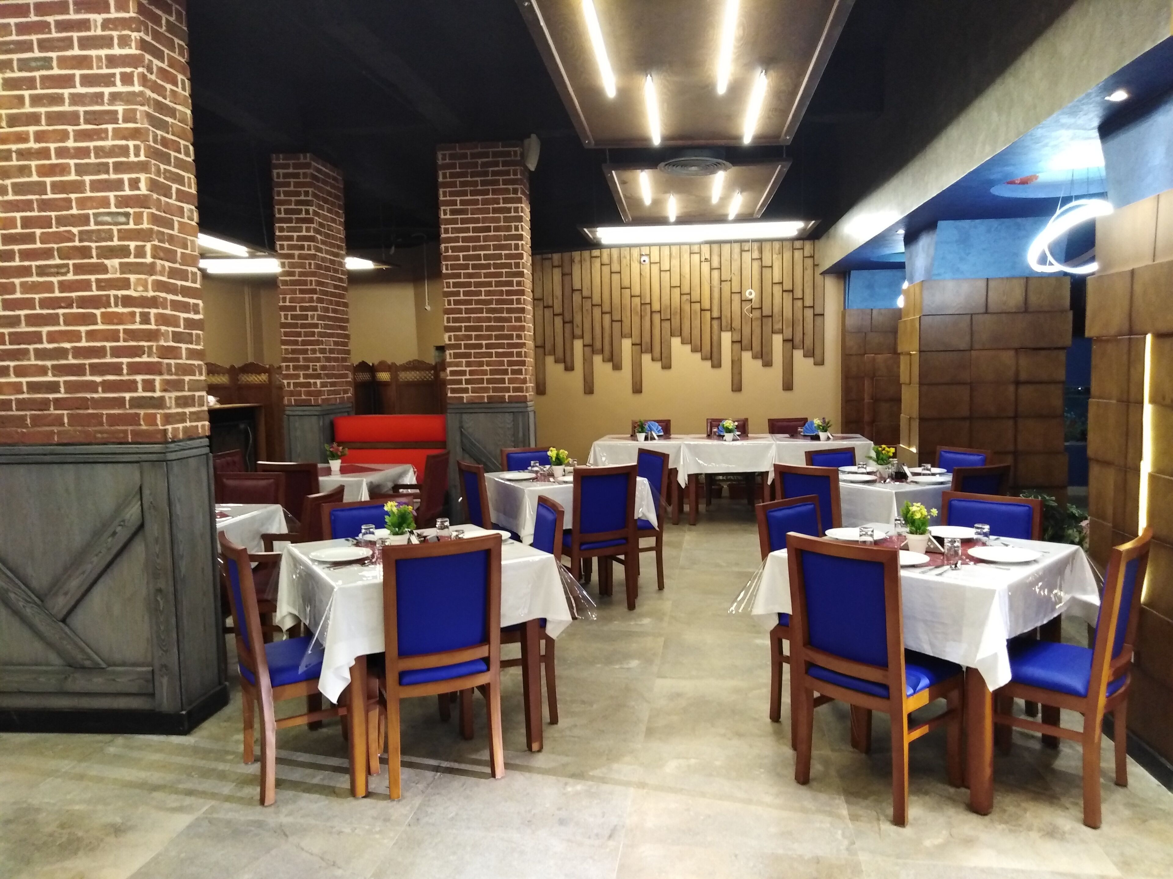 A restaurant interior with brick pillars, wooden walls, and tables set with blue chairs and white tablecloths.