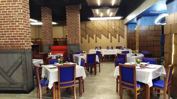 A restaurant interior with brick pillars, wooden walls, and tables set with blue chairs and white tablecloths.