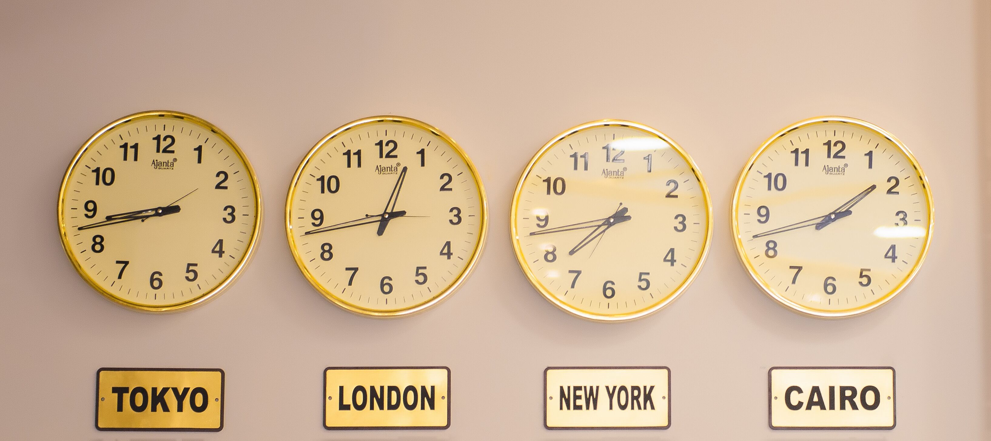 Quatre horloges murales affichant des fuseaux horaires différents, avec les noms des villes correspondantes indiqués en dessous : Tokyo, Londres, New York et Le Caire.
