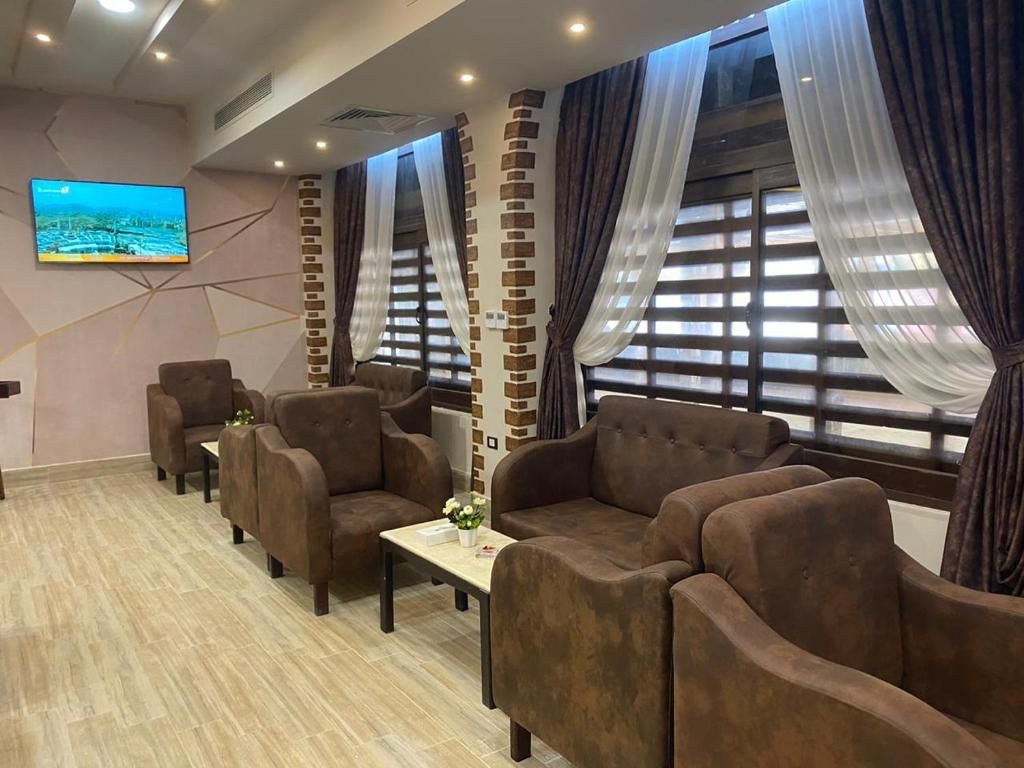 A hotel room with a sofa set, a flat-screen TV, and a window with curtains.