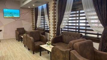 A hotel room with a sofa set, a flat-screen TV, and a window with curtains.