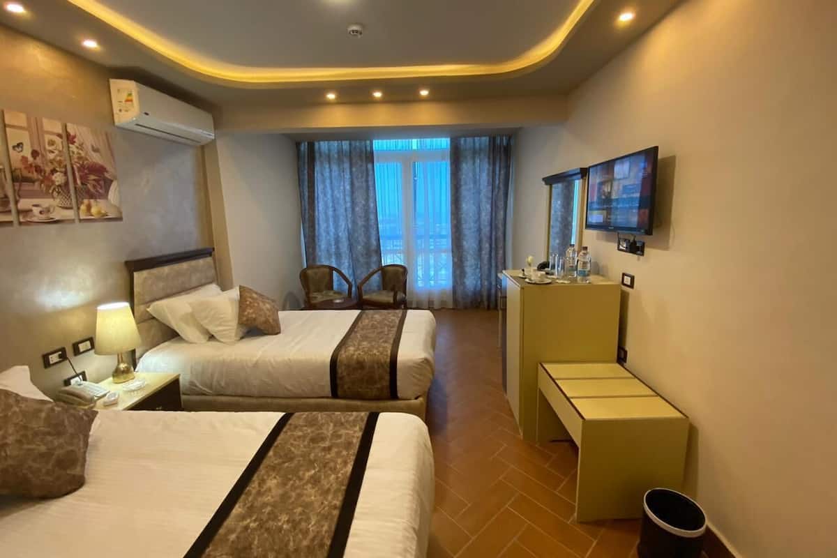 A hotel room with two beds, a desk, a TV, and a window with curtains.