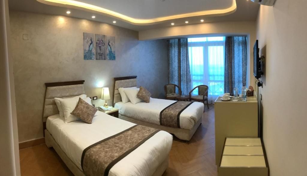 Habitación de hotel con dos camas, un escritorio, sillas, un televisor y una ventana con cortinas.