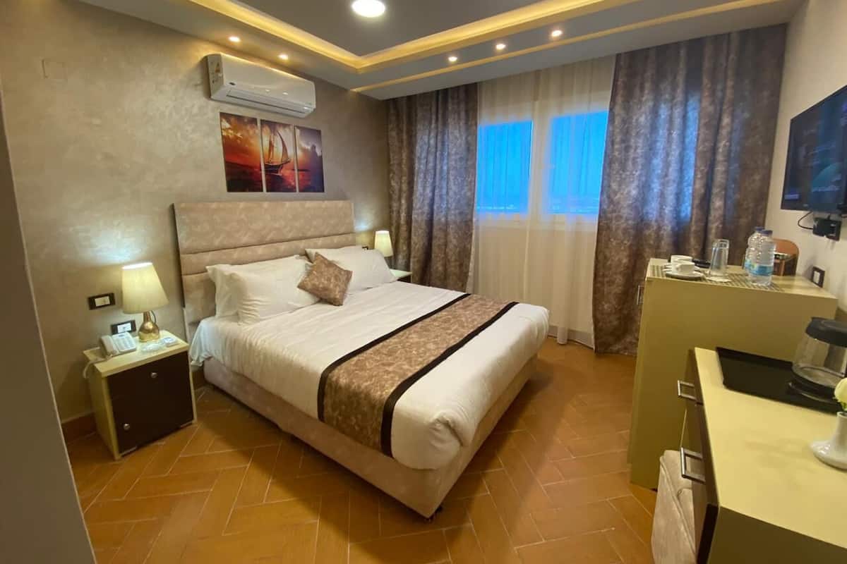 A hotel room with a bed, bedside tables, a desk, and a window with curtains.