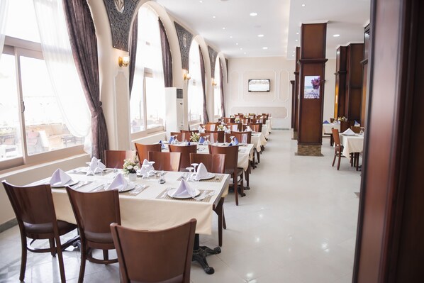 A restaurant with long tables, chairs, and a large window with curtains.
