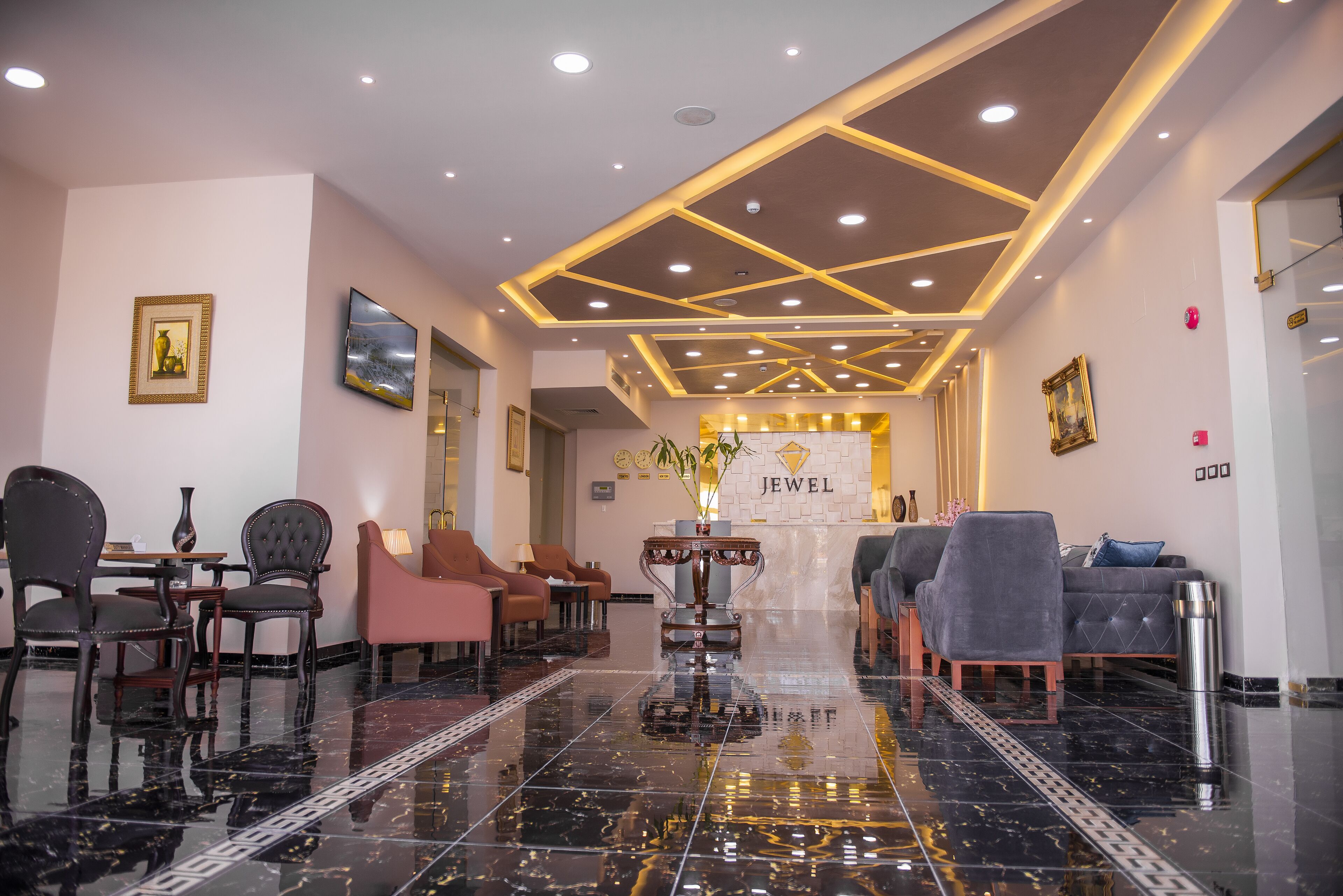 Um saguão de hotel com piso de mármore polido, áreas de estar e uma recepção com a placa 'Jewel'.