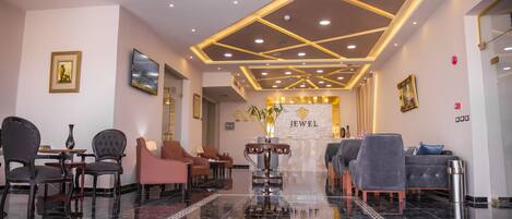 Um saguão de hotel com piso de mármore polido, áreas de estar e uma recepção com a placa 'Jewel'.