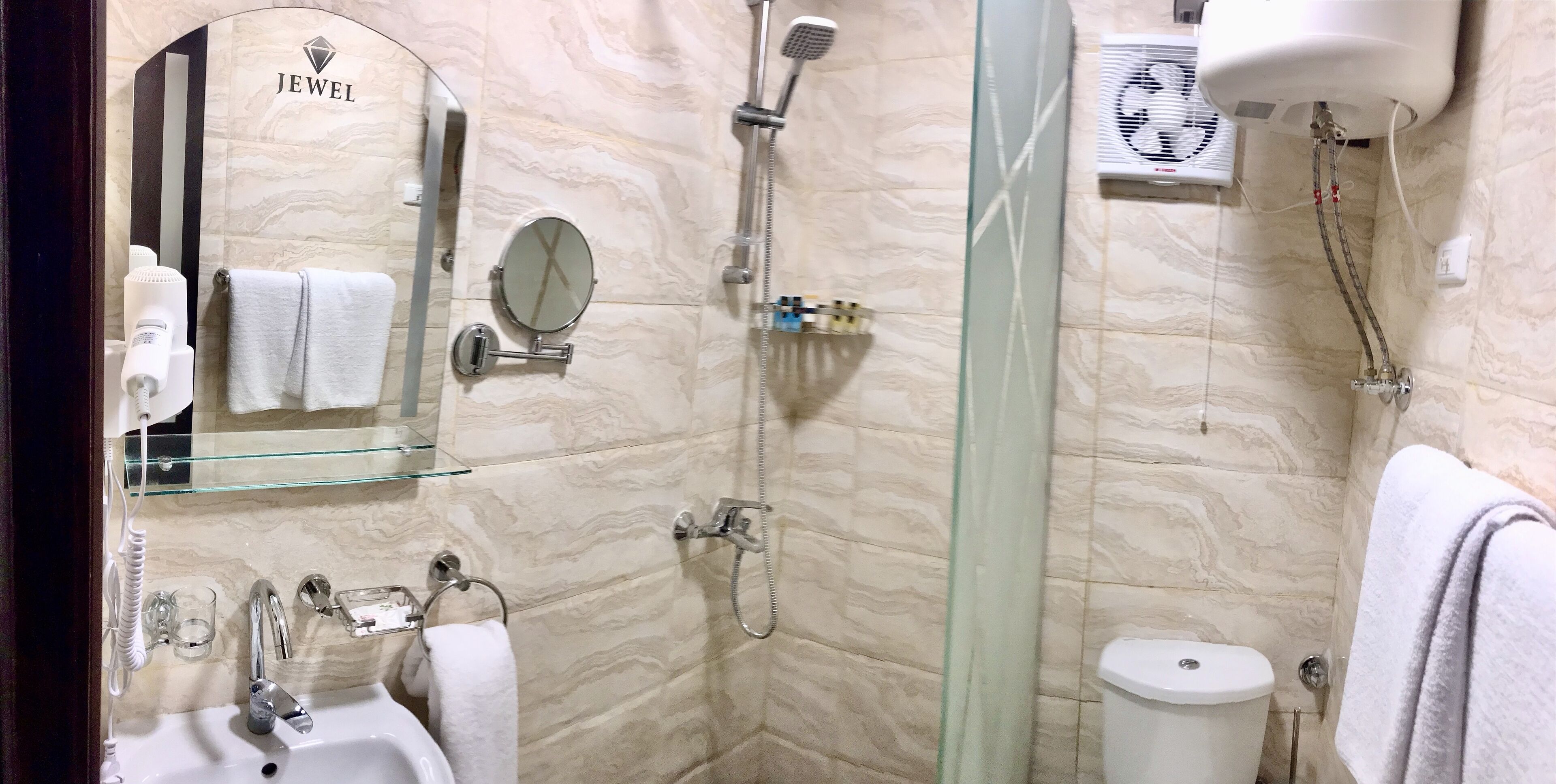 A bathroom with a marble wall, a glass shower enclosure, a toilet, a sink, a mirror, and a towel rack.