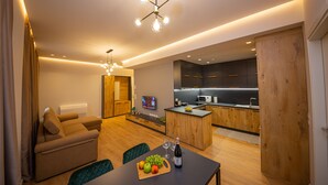 A modern living room with a sofa, dining table, and a kitchen area with wooden cabinets and a built-in oven. - Central Chic Apartments (Tirana)