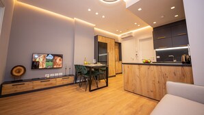 A modern kitchen with wooden cabinets, a dining area with a table and chairs, and a TV mounted on the wall. - Central Chic Apartments (Tirana)