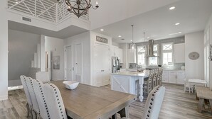 Een ruime keuken met een centraal eiland, witte kasten en een eethoek met een houten tafel en gestoffeerde stoelen.