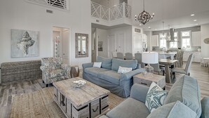 Een ruime woonkamer met een grote bank, een salontafel en een eetgedeelte met een kroonluchter.