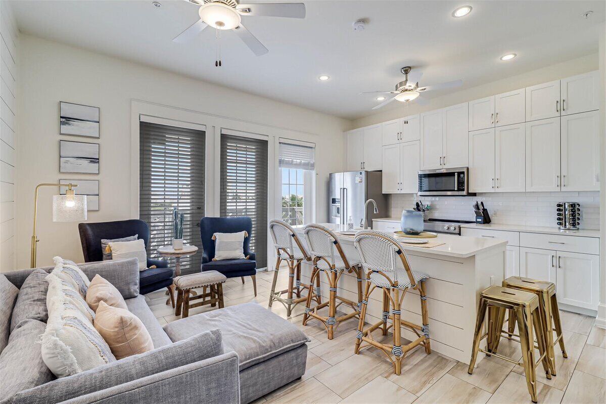 A modern kitchen with white cabinets, a central island, and a dining area with wicker chairs.