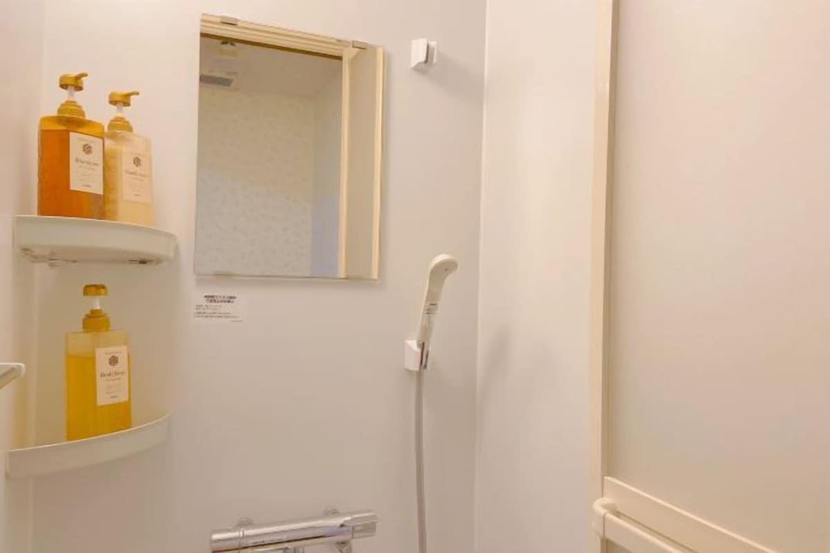 Un baño con ducha, espejo y repisas con artículos de aseo.
