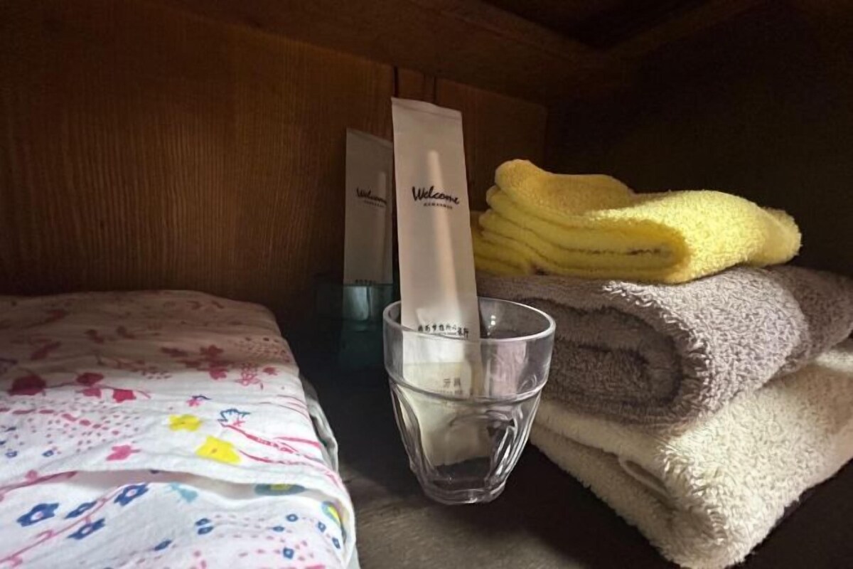 A bed with a floral-patterned bedspread, a glass of water, and a stack of towels.