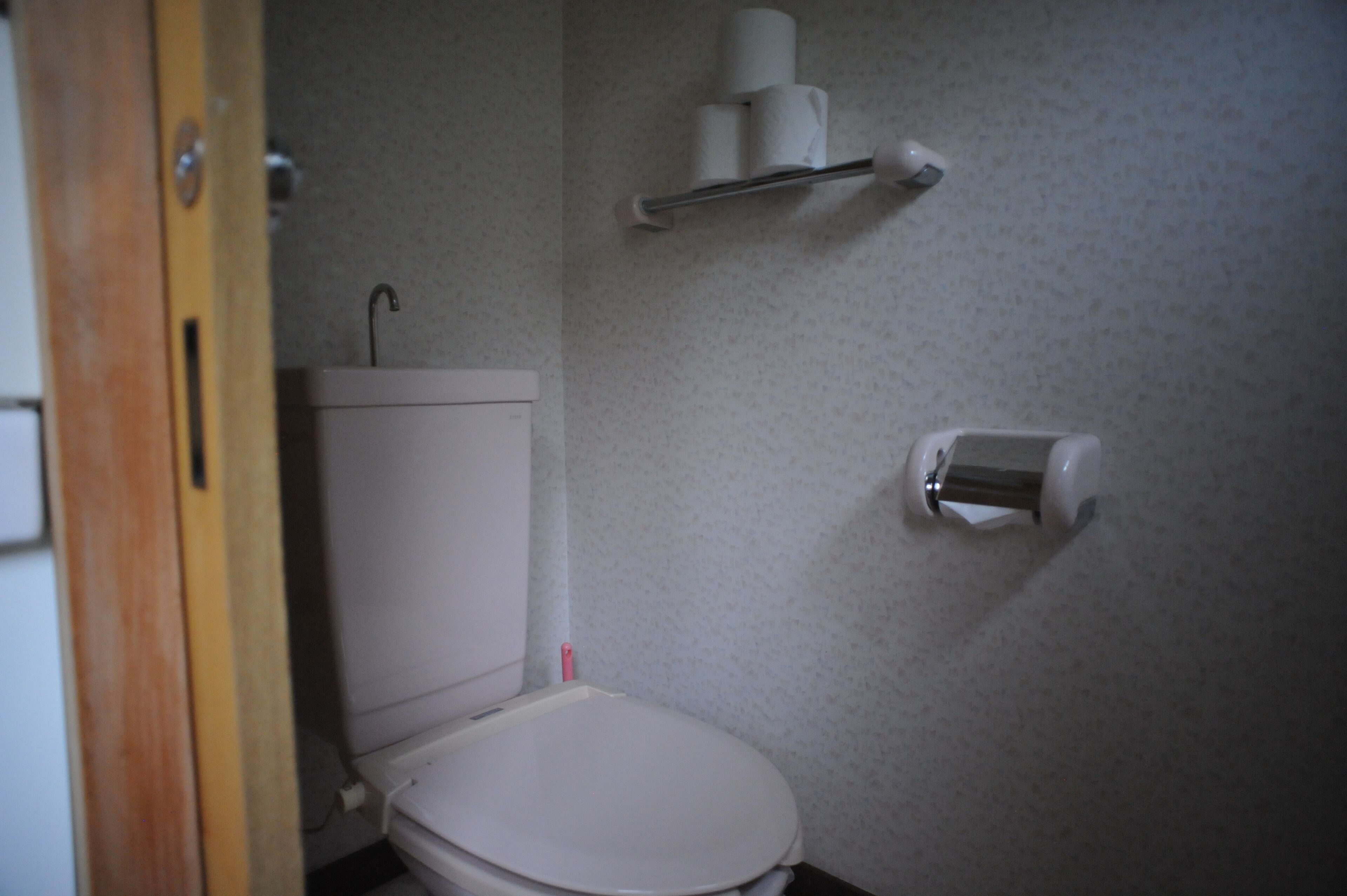 A small bathroom with a toilet, a toilet paper holder, and a paper towel dispenser.