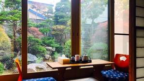 A traditional Japanese room with tatami flooring, a low wooden table, and a view of a garden through a sliding door.