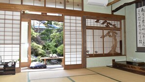 A traditional Japanese room with tatami flooring, shoji screens, and a view of a garden.