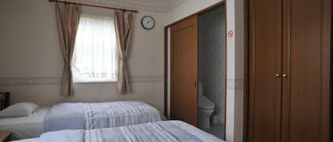 Habitación de hotel con dos camas, una ventana con cortinas, un reloj, un inodoro y un armario.