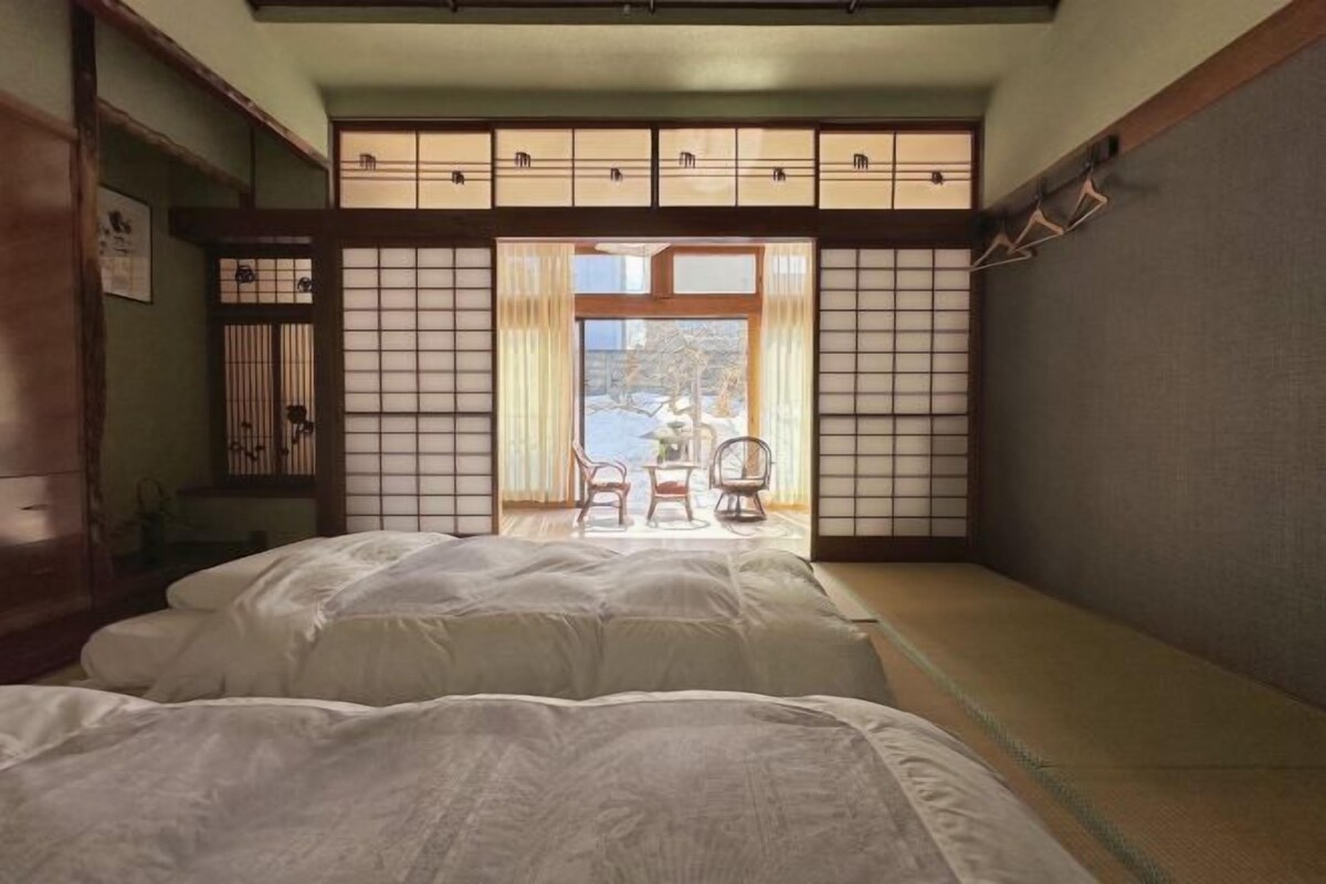 Een traditionele Japanse kamer met tatami vloerbedekking, een laag bed, een schuifdeur en uitzicht op de omgeving.