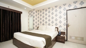 A bedroom with a large bed, a nightstand, a wardrobe, and patterned wallpaper. - Hotel Opera Inn near Central Bus Stand (Udaipur)