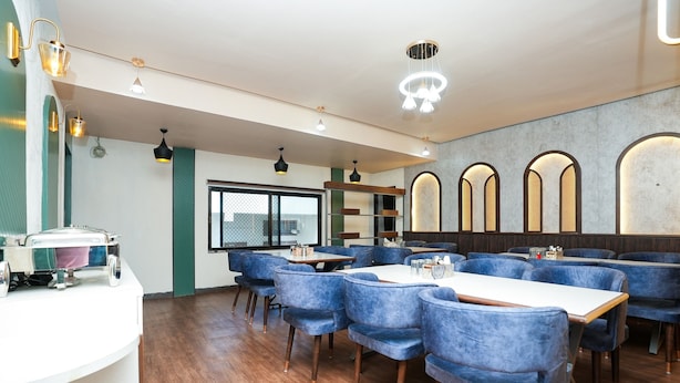 A restaurant with blue upholstered booths, wooden tables, and pendant lighting. - Hotel Opera Inn near Central Bus Stand (Udaipur)