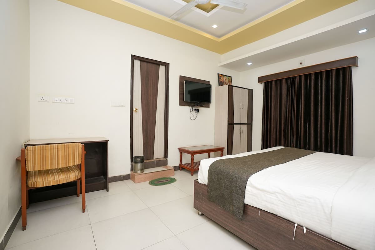 Quarto de hotel com cama, escrivaninha, cadeira, televisão e guarda-roupa.