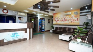A hotel reception area with a reception desk, a clock, an air conditioning unit, a Pepsi refrigerator, a large wall mural, and a seating area with a sofa and a coffee table. - Hotel Opera Inn near Central Bus Stand (Udaipur)