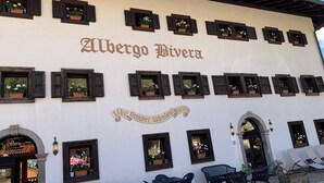 A building with the sign "Albergo Biviera" and a banner reading "liti semper splendidus". There are outdoor tables and chairs, and a bar/lounge area is visible. - Hotel Bivera Sauris (Sauris)