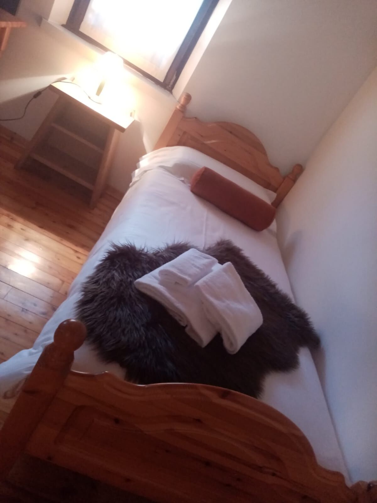 A small, narrow room with a wooden bed, white bedding, and a dark furry rug.