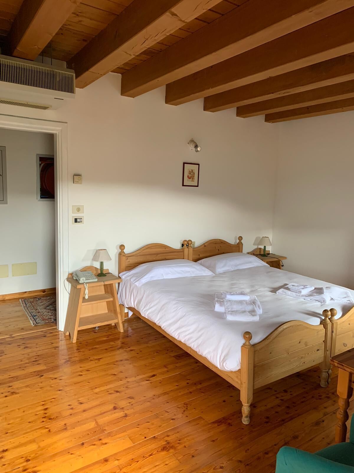 Una cama de madera con ropa blanca de cama, una mesita de noche con una lámpara y un pequeño cuadro en la pared.