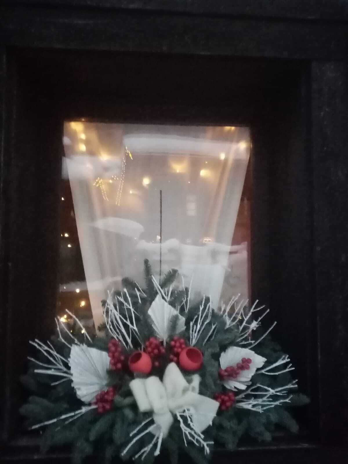 Una guirnalda navideña con adornos blancos y rojos en un ventanal.