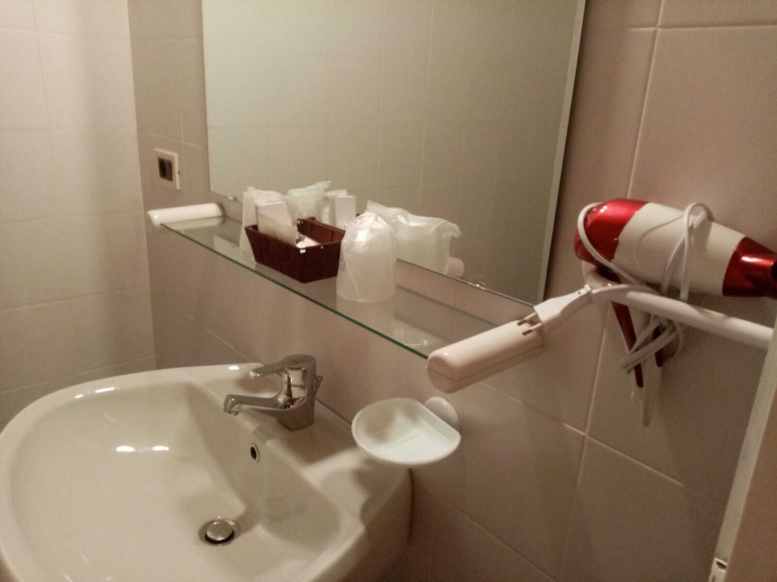 A bathroom with a white sink, a glass shelf with toiletries, and a red and white hairdryer on a white towel rack.
