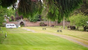 Un parco con tavoli da picnic e un camper bianco parcheggiato vicino a un muro in mattoni.