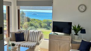 A modern living room with a large window, a flat-screen TV, and a view of the sea. - Promenade 12, 8 Intrepid Cl - fantastic waterfront unit with air con and Wifi (Nelson Bay)