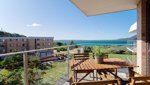 A balcony with a wooden table and chairs, overlooking a coastal view with buildings and greenery. - Promenade 12, 8 Intrepid Cl - fantastic waterfront unit with air con and Wifi (Nelson Bay)