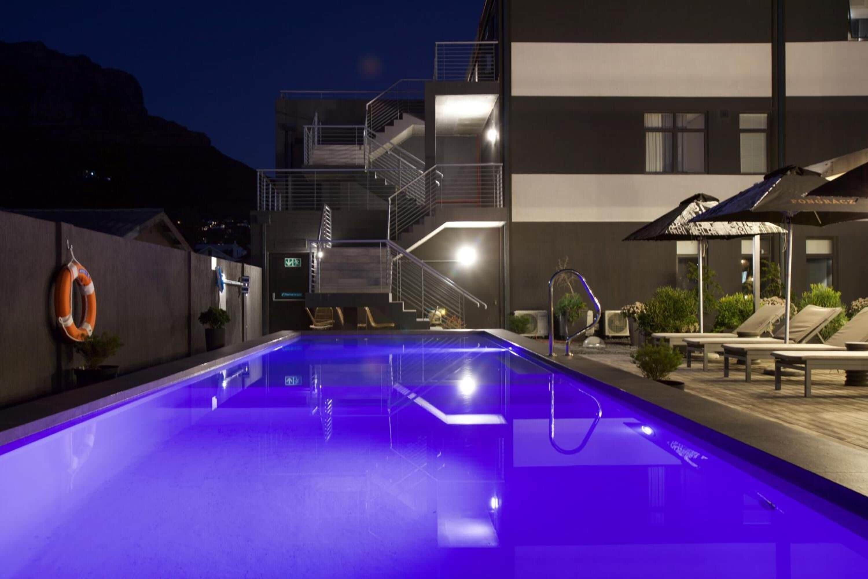 Una piscina con luz azul, un flotador salvavidas y una escalera que lleva a un nivel superior.