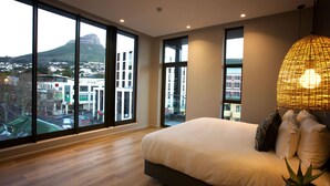 Een moderne slaapkamer met een groot bed, een plant in pot en een uitzicht op een stadsgezicht door grote ramen.