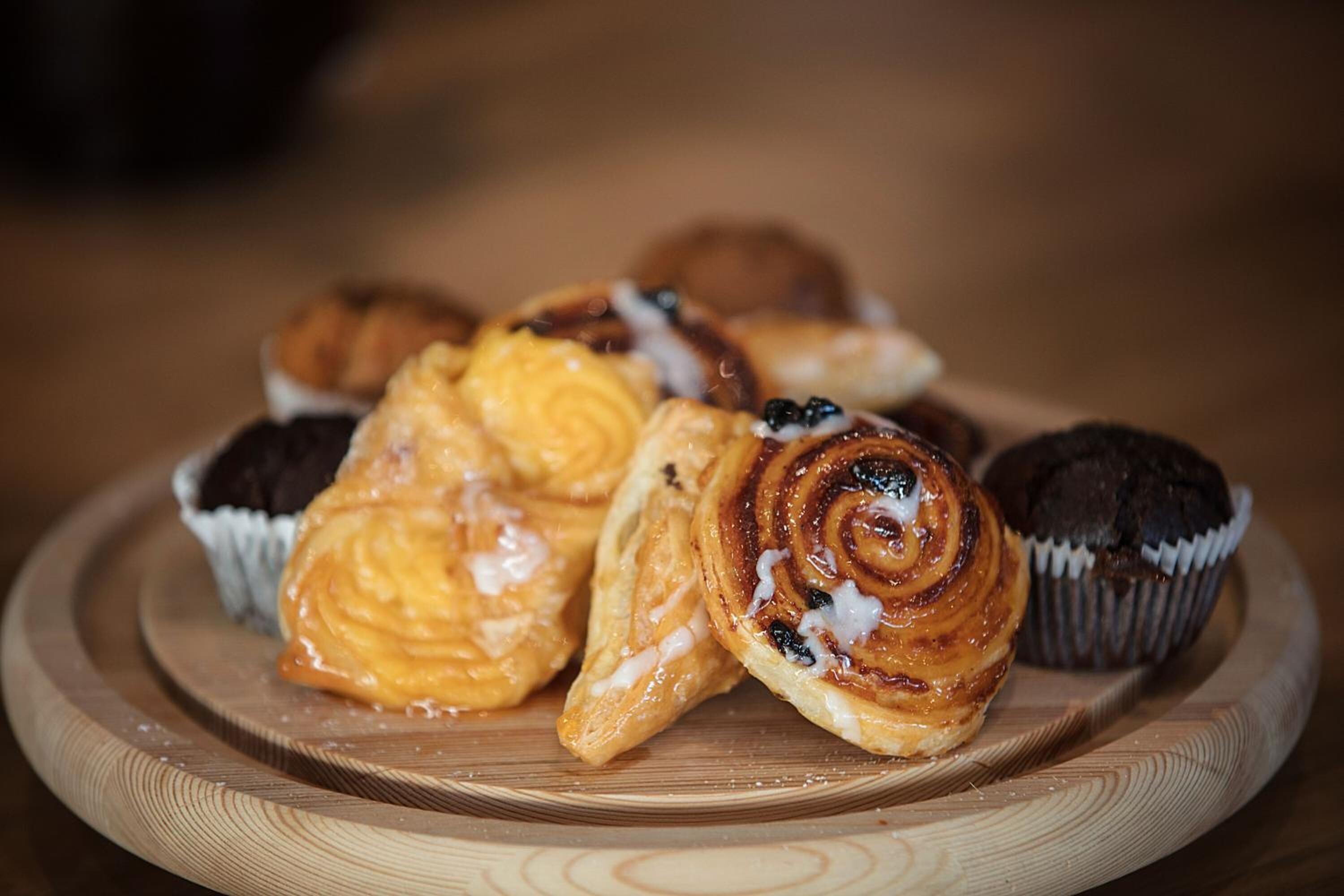 A wooden tray with various pastries, including a cinnamon roll and a chocolate muffin.
