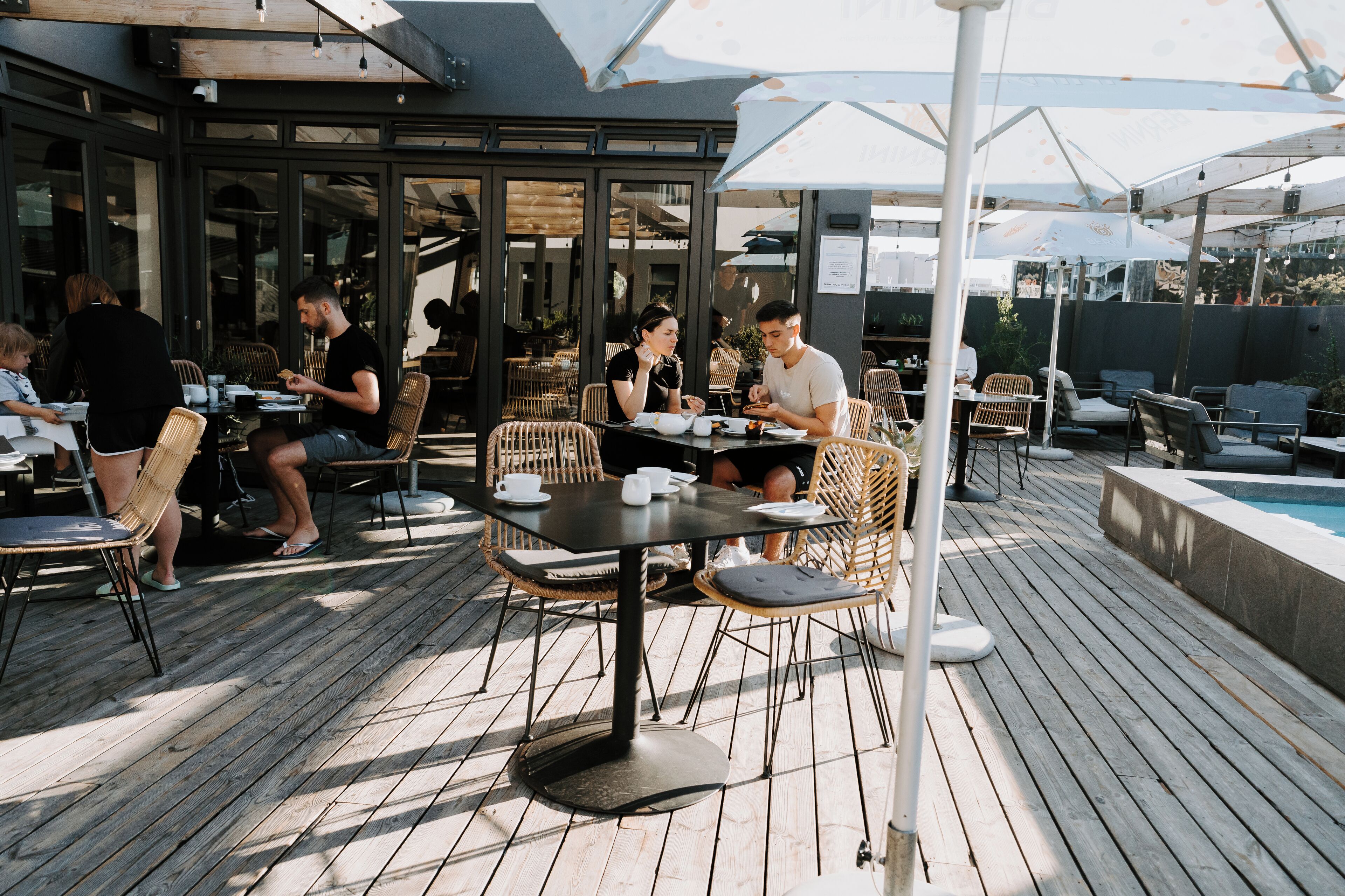 An outdoor dining area with tables and chairs, a pool, and umbrellas.