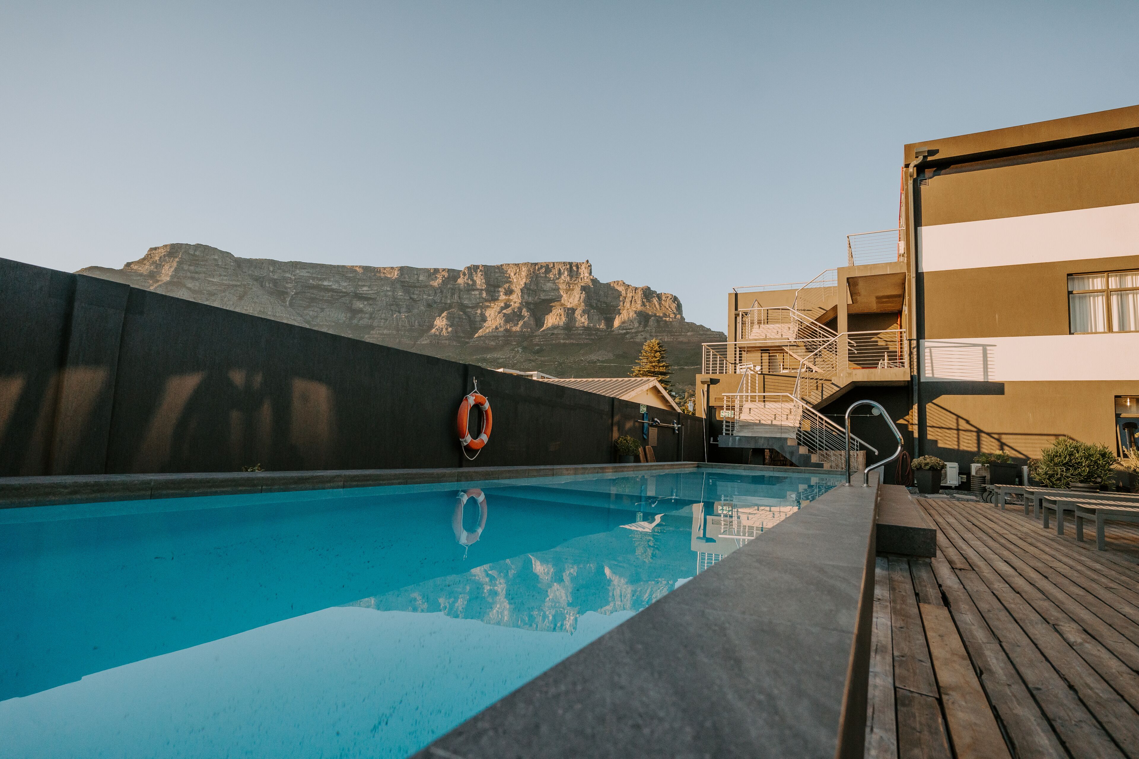 A swimming pool with a lifebuoy, wooden deck, and a building with a staircase.