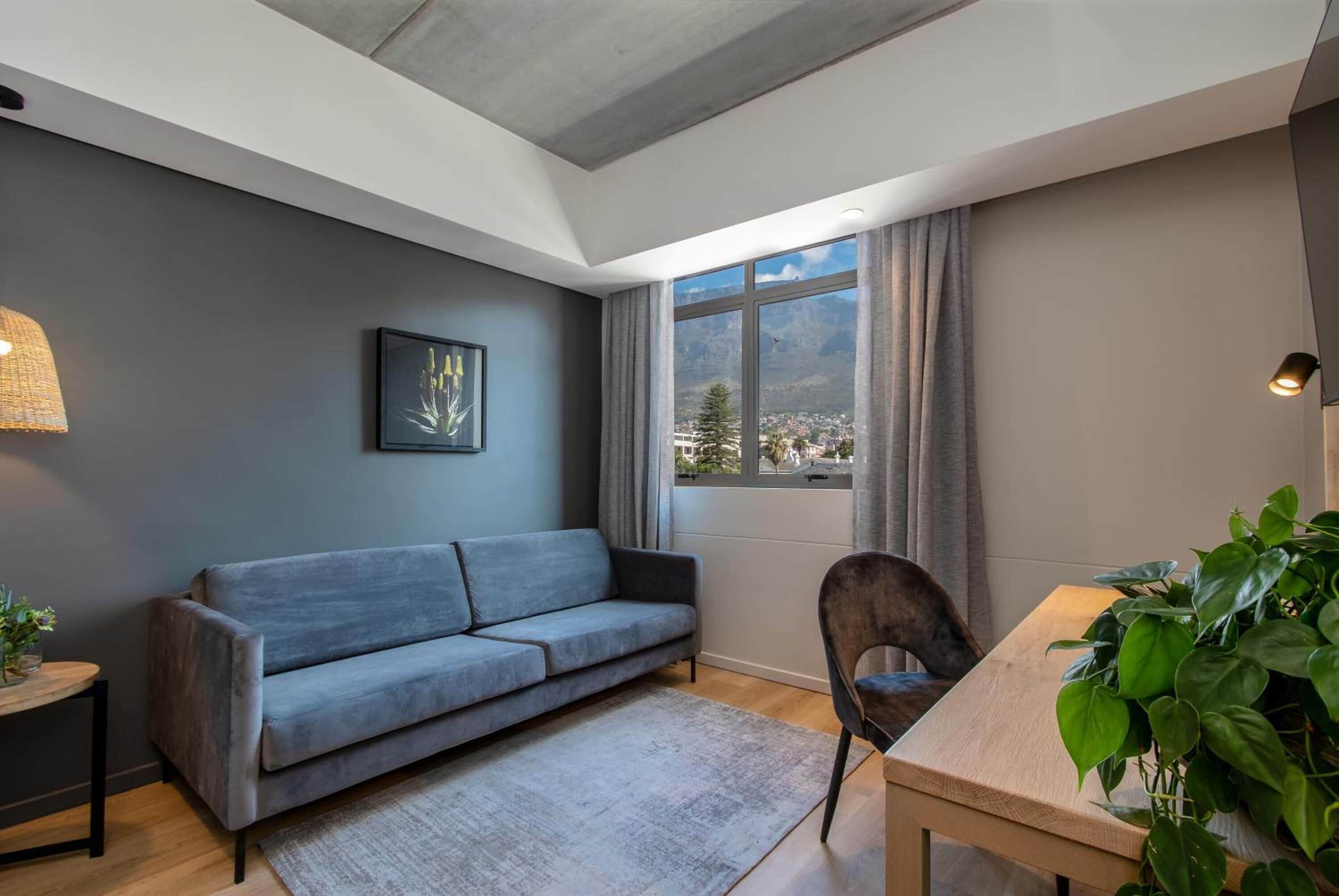 Una sala de estar moderna con un sofá gris, una mesa de comedor de madera y un amplio ventanal con vistas a un paisaje montañoso.