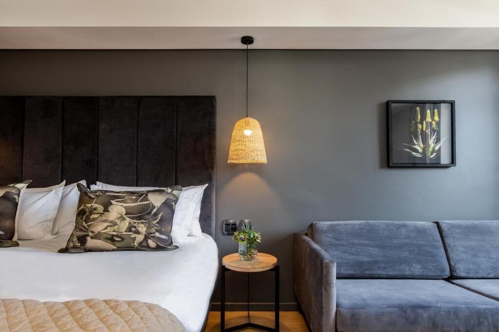 A modern bedroom with a large bed, a grey sofa, a hanging light fixture, and a framed picture on the wall.