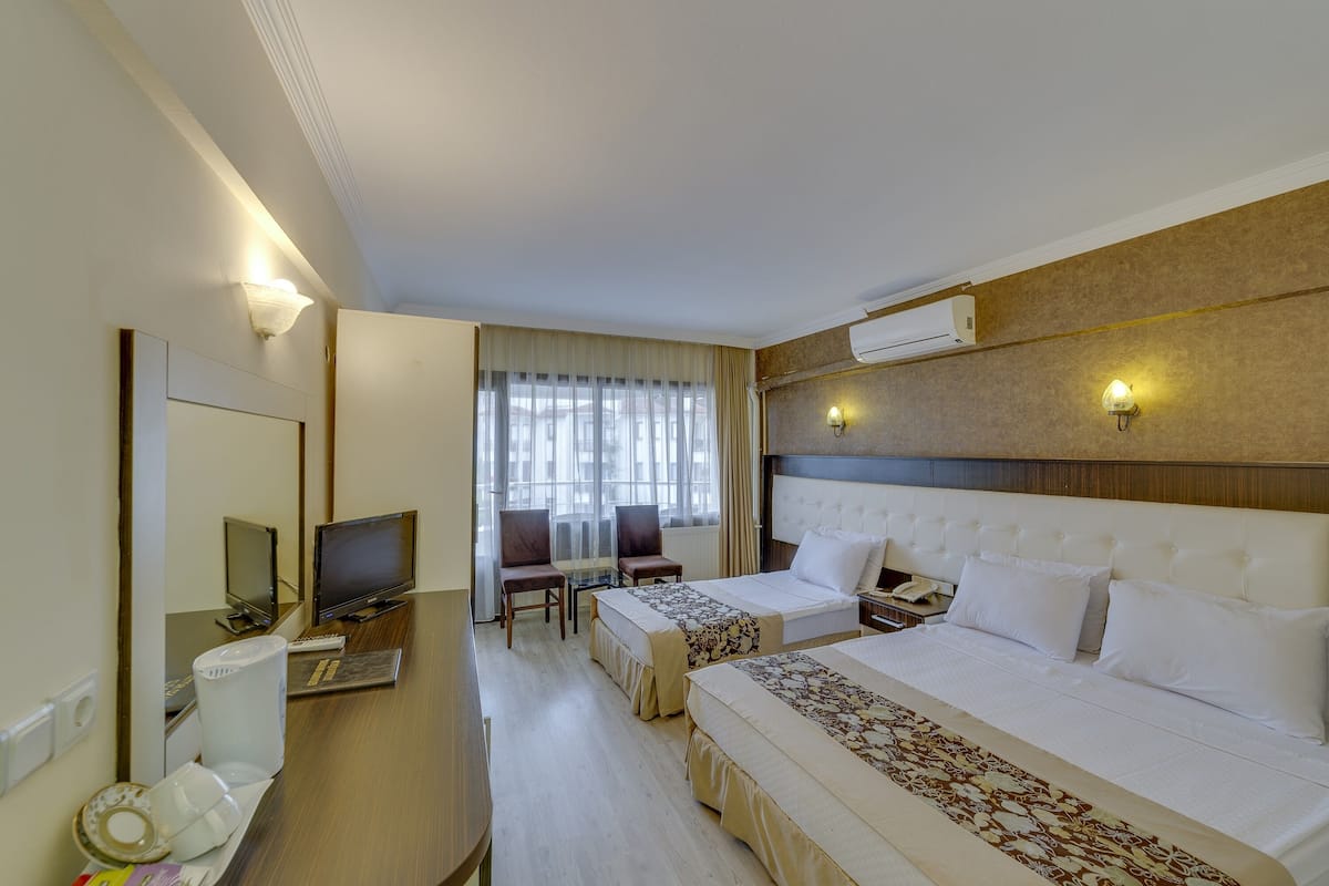 Ein Hotelzimmer mit zwei Betten, einem Schreibtisch mit Computer, einem Fernseher und einem Fenster mit Vorhängen.