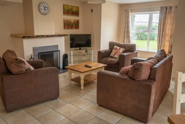 A living room with brown sofas, a wooden coffee table, a flat-screen TV, and a fireplace. - House 3 Dingle Manor Remarkable 3-bed House (Dingle)
